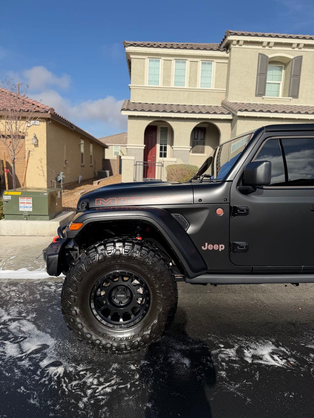 Black Jeep Wrangler parked in residential area, with soap suds on the road after washing.